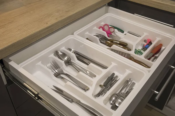 Opened kitchen drawer with a tray and cutlery inside. Grey front of the drawer, white inside, handless design.