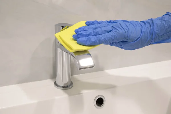 Person hand In blue glove cleaning silver basin mixer and white sink