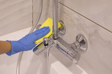 İnsan eli Mavi eldivenle gümüş küveti ve beyaz lavaboyu temizler