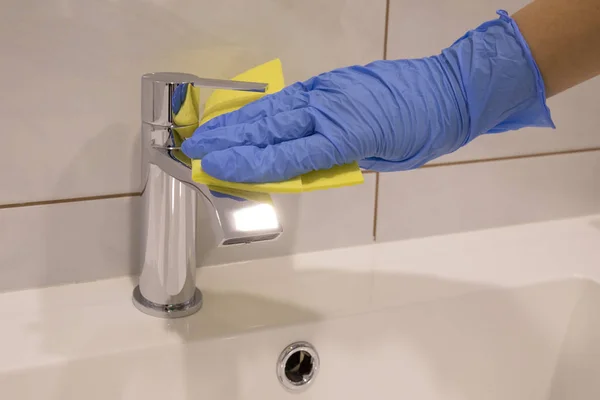 Person hand In blue glove cleaning silver basin mixer and white sink