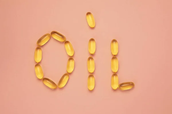 Alimentación dieta estilo de vida saludable. Cápsulas amarillas con suplementos de aceites vegetales y de pescado en palabra aceite sobre fondo rosa — Foto de Stock