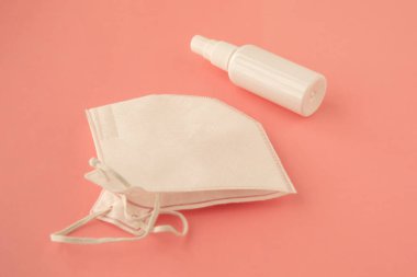 Beyaz şişedeki antibakteriyel spreyi ve koruyucu maskeyi temizliyorum. Coronavirus önleme kavramı.