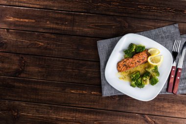 Brokoli ve kireç ile beyaz bir tabak ta ızgara alabalık biftek. Ahşap arka planda çatal bıçak takımı. Metin için boş alan