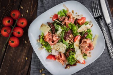 Prosciutto ve parmesanlı salata. Masada vişne, domates, çatal, bıçak ve çam fıstığı var. Düz yatay fotoğraf