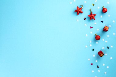 Noel ve kış kompozisyonu. Beyaz kar tanelerinden yapılmış çerçeve ve pastel mavi arka planda kırmızı oyuncaklar. Noel, kış, yeni yıl konsepti. Düz konum, üst görünüm, kopyalama alanı