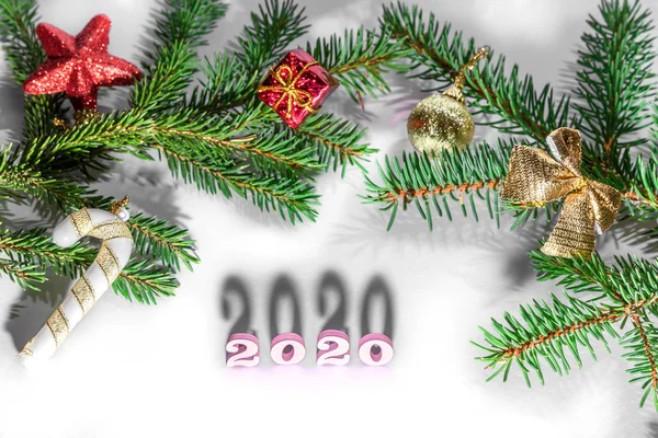 Diseño creativo de números 2020 hecho de figuras de color rosa pastel de madera sobre fondo blanco con sombras de rama de abeto y juguetes rojos. Concepto de Año Nuevo con espacio de copia para nota y texto —  Fotos de Stock