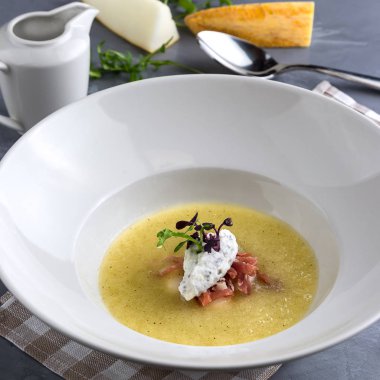 Naneli kavun çorbası, proshuto ve salatalık. Beyaz tabak, tencere, gri arka planda kaşık. Yakın plan.