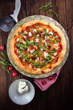 Manzaralı pizza, mozarella, domates ve taze fesleğen. Pizzacı ve pembe masa örtüsü ahşap arka planda yatıyor. Dikey düzlük. Geleneksel İtalyan fast food