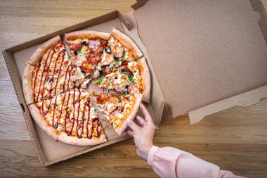 Kadın karton kutudan lezzetli bir pizza dilimi alıyor. Kahverengi ahşap masanın üstü..