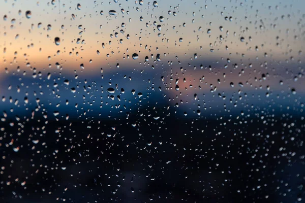 Texture of water drops after rain on glass with sunset outside the window. Blurred sun and sky, beautiful dusk, rainy weather — Stock Photo, Image