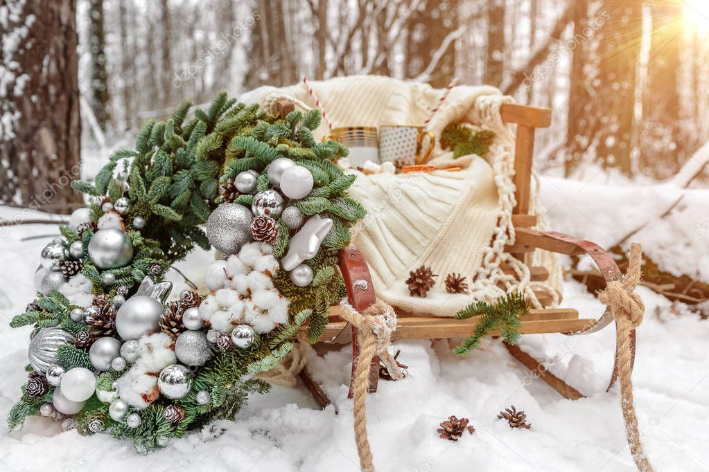 Winter Christmas decoration in forest. Old vintage sled and green wreath of fir branches with cones in the snow