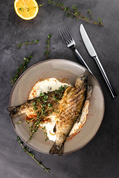 Limon soslu kızarmış gökkuşağı alabalığı ve arka planda siyah mermer masa üzerinde kekik. Üst görünüm