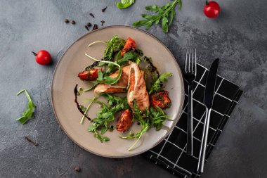 Kırsal tarzda gri çimento arka planda güzel bir yemek, fırında domatesli rulo köfte ve restoranda bej tabakta yeşil roka, üst manzara.