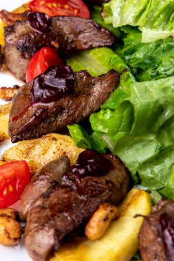 Karaciğer salatası ve kızarmış kaju fıstıklı yemek kompozisyonu. Arugula, domates, beyaz tabakta patates. Makro görünüm