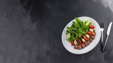 Rozbif salatası, güneşte kurutulmuş domates roka, domates ve salatalık, gri arka planda. Kopyalama alanı olan yiyecek kavramı.