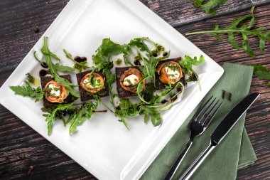 Pastırmalı tavuk dürümleri ve kızarmış ekmeğin üstüne roka. Koyu ahşap zemin üzerinde beyaz kare plaka