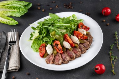 Güneşte kurutulmuş domatesli biftek salatası. Arugula, domates ve salatalık beyaz tabakta, yakın plan gri.