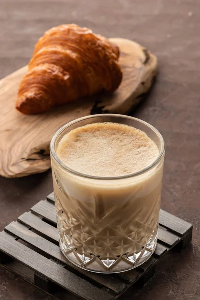 Xícara de cappuccino café em vidro transparente com croissant fresco francês, velho fundo enferrujado — Fotografia de Stock