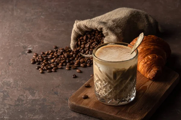 Xícara de cappuccino de café em vidro transparente com croissant fresco francês, grãos de café torrados em um saco, fundo enferrujado velho com espaço de cópia — Fotografia de Stock