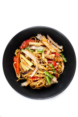 Dilimlenmiş tavuk göğsü, soslu erişte, sebze ve susam tohumları beyaz arka planda izole edilmiş siyah bir tabakta.