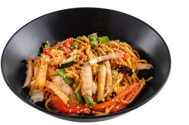 Dilimlenmiş tavuk göğsü, soslu şehriye, sebze ve susam tohumları beyaz arka planda izole edilmiş siyah bir tabakta.