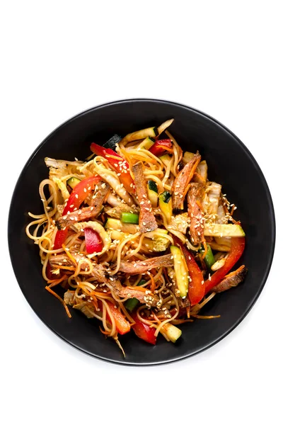 Sliced beef, noodles in sauce, vegetables and sesame seeds in a black plate isolated on white background — Stock Photo, Image