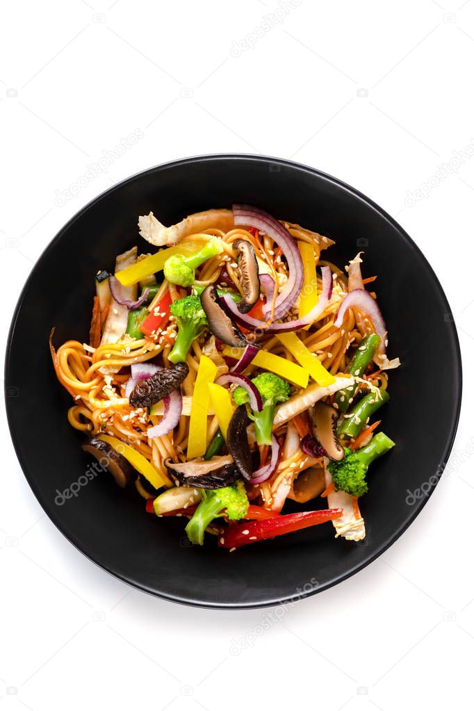Sliced grilled vegetables, noodles in sauce, sesame seeds in a black plate isolated on white background, top view