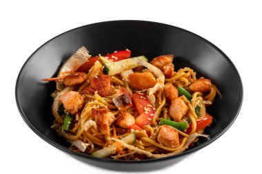 Dilimlenmiş somon bifteği ve sebze karışımı, soslu şehriye, kırmızı biber, beyaz arka planda izole edilmiş siyah tabakta susam tohumu.