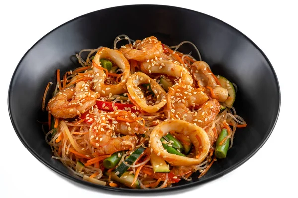 Grilled king prawns, squid rings and vegetables mix, noodles in sauce, red pepper, sesame seeds in a black plate isolated on white background, side view — Stock Photo, Image