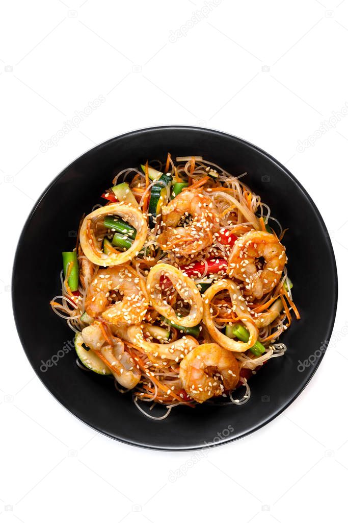 grilled king prawns, squid rings and vegetables mix, noodles in sauce, red pepper, sesame seeds in a black plate isolated on white background, top view