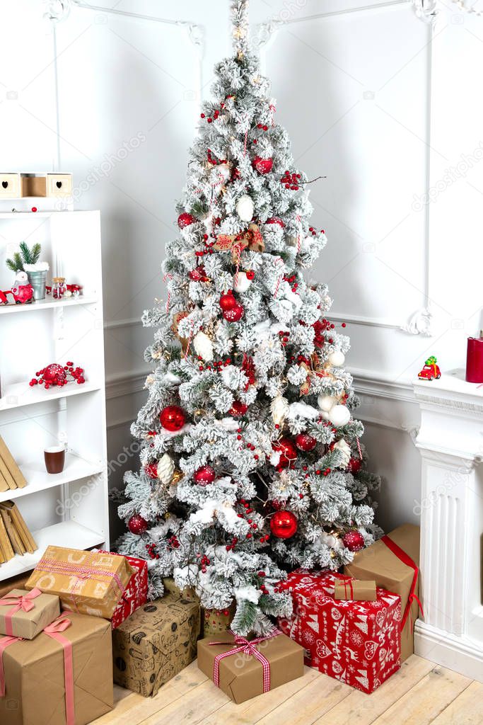 Interior of a beautiful white room decorated for Christmas, a lot of gift boxes and presents under a snow covered fir tree, festive mood atmosphere and concept of New Year