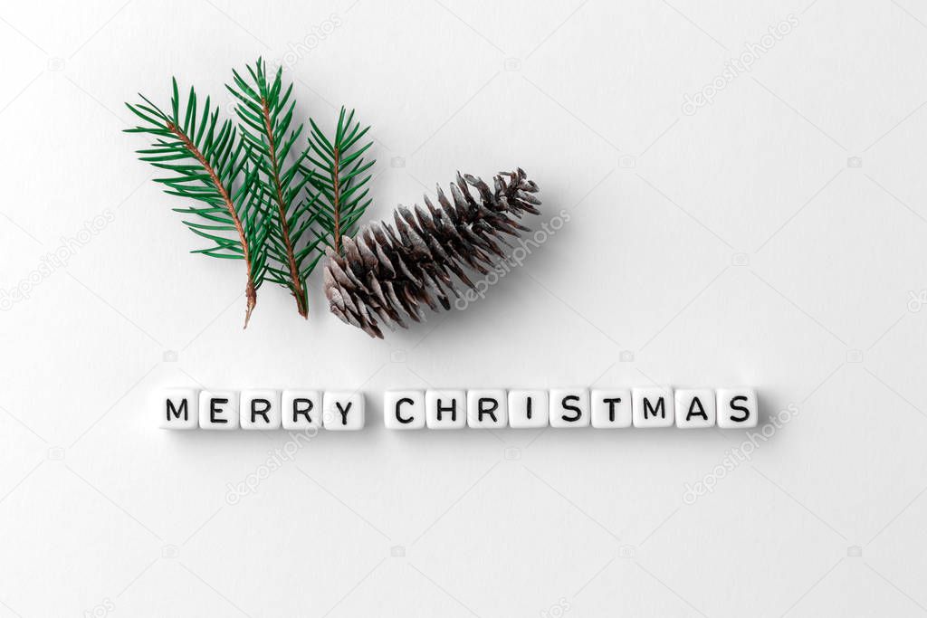 Creative layout of words merry christmas made of wooden cubes with letters on white paper background, New Year minimalistic concept with fir cones and green branches with needles