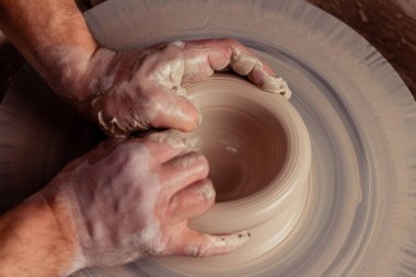 Kirli çömlekçinin ellerine yakından bak parmaklarıyla ve basınçla stüdyodaki çömlekçinin tekerlek çemberinde toprak kavanozu dolusu beyaz kil yaratıyor.