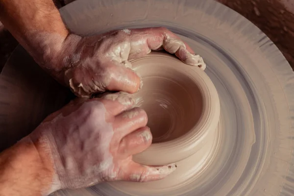Close-up view on dirty man hands of potter creating with fingers and pressure an earthen jar pot of white clay on the potter's wheel circle in studio — Stock Photo, Image