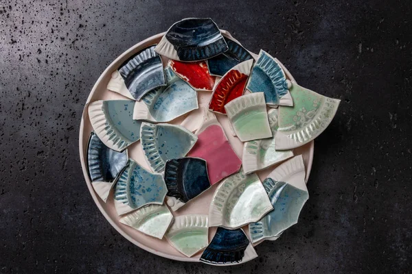 Multicolor shards of broken ceramic dishes on a white tray, gray stone background with copy space — Stock Photo, Image