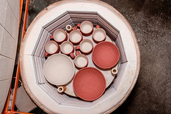 Skládané keramické misky, hrnce, nádobí a hrnky, hliněné ruční výrobky před pečením v muflovací peci v hrnčířském ateliéru — Stock fotografie
