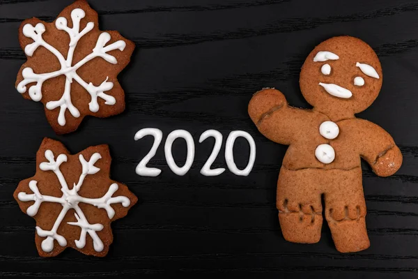 Concepto mininalístico de Navidad y año nuevo sobre fondo de madera negro con figuras 2020 hechas con glaseado blanco y pan de jengibre casero hombre, vista superior —  Fotos de Stock