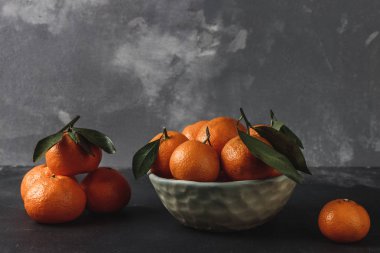 Taze toplanmış yeşil yapraklı mandalinalar gri çimento arka planında, kış zamanı meyveleri ve Noel ve yeni yılın sembolü.