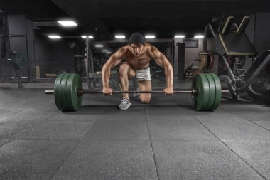 Spor salonunda halter egzersiziyle ayakta duran güçlü atletik adamın ön görüntüsü.