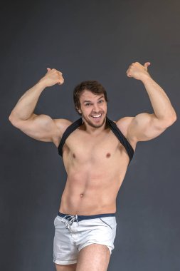 Güçlü kaslı atletik vücut geliştirici ya da formda model iki elle hareket, gülümseme ve gri duvarın yanında poz veriyor.