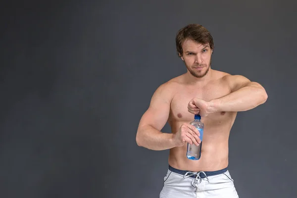 Bodybuilder athlétique fort musculaire en essayant d'ouvrir une bouteille d'eau et en regardant la caméra. Concept photo sport avec fond mural gris et espace de copie pour le texte — Photo