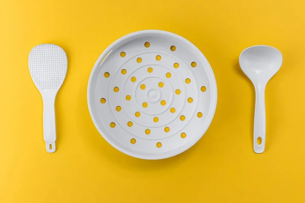 White plastic kitchen spatula and colander on a yellow background, concept of food and kitchenware with copy space, top view — Stok fotoğraf