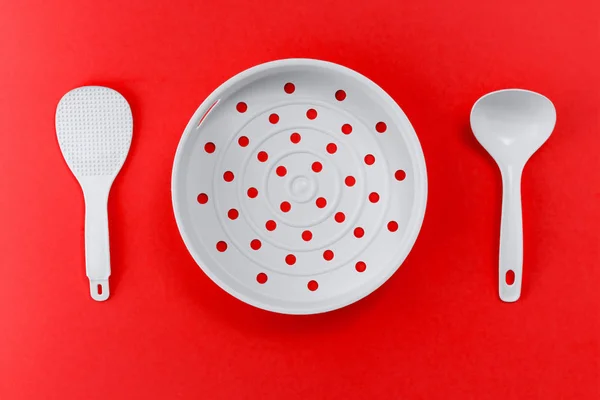 White plastic kitchen spatula and colander on a red background, concept of food and kitchenware with copy space, top view — Stock Photo, Image