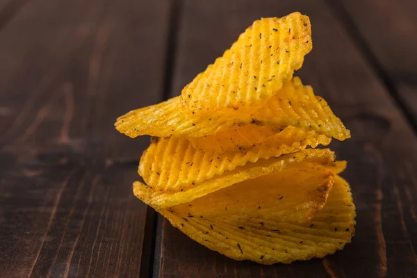 Een bos van golvende gouden chips op bruine houten achtergrond, close-up zicht op fast food — Stockfoto