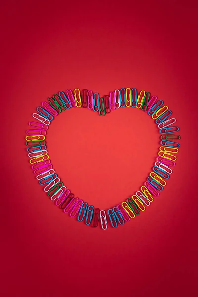 Rainbow-colored paper clips layout as a big heart on red paper background, creative LGBT concept for valentine's day or wedding, flat lay, top view, copy space — Stok fotoğraf