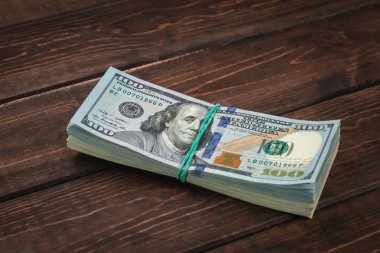Kahverengi ahşap arka planda yeşil elastik bantla bağlanmış yüz dolarlık banknotların yakın plan yığını, bir tomar para bir iş ve finans kavramı