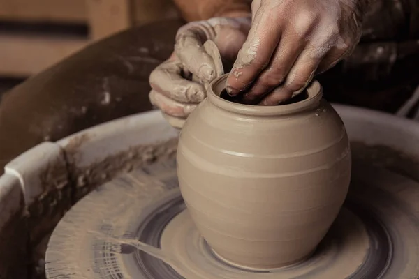 Close-up view on dirty man hands of potter creating with fingers and pressure an earthen jar pot of white clay on the potter's wheel circle in studio — ストック写真