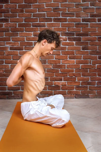 young man showing breathing practices of belly, abdominal vacuum exercise. Yoga concept with copy space on brown brick wall background