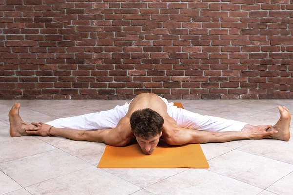 Sporty man practicing hatha yoga in studio. Male in white pants sitting in Wide-Angle Forward Bend pose, Upavishtha Konasana. Yogi, sport and healthy concept with copy space — Stock Photo, Image