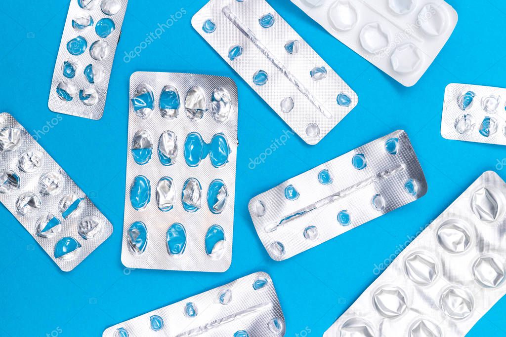 Many empty packs of pills sparkling on blue background, concept of drug abuse with copy space, top view